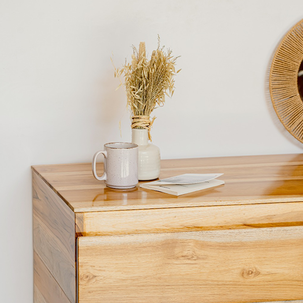 Wooden side table with a white mug, small vase with dried plants on it 