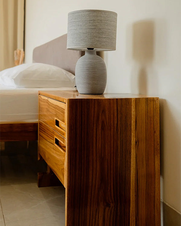 Gray textured lamp on a wooden bedside table next to a bed