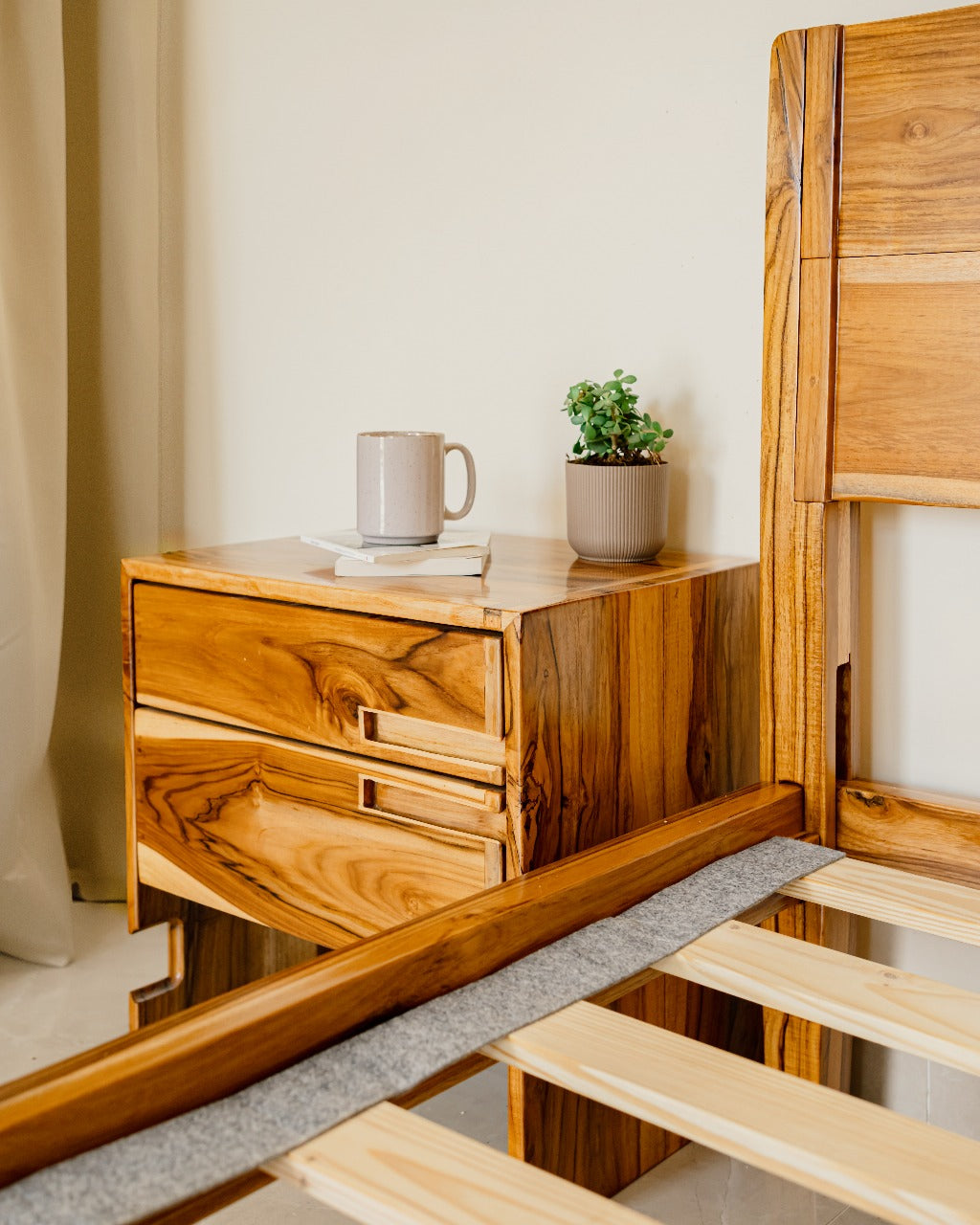 Wooden bedside with a mug and plant beside a bed.