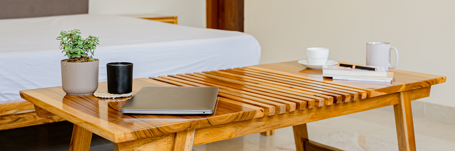 Wooden coffee table with a laptop, cups, and books in a bedroom setting